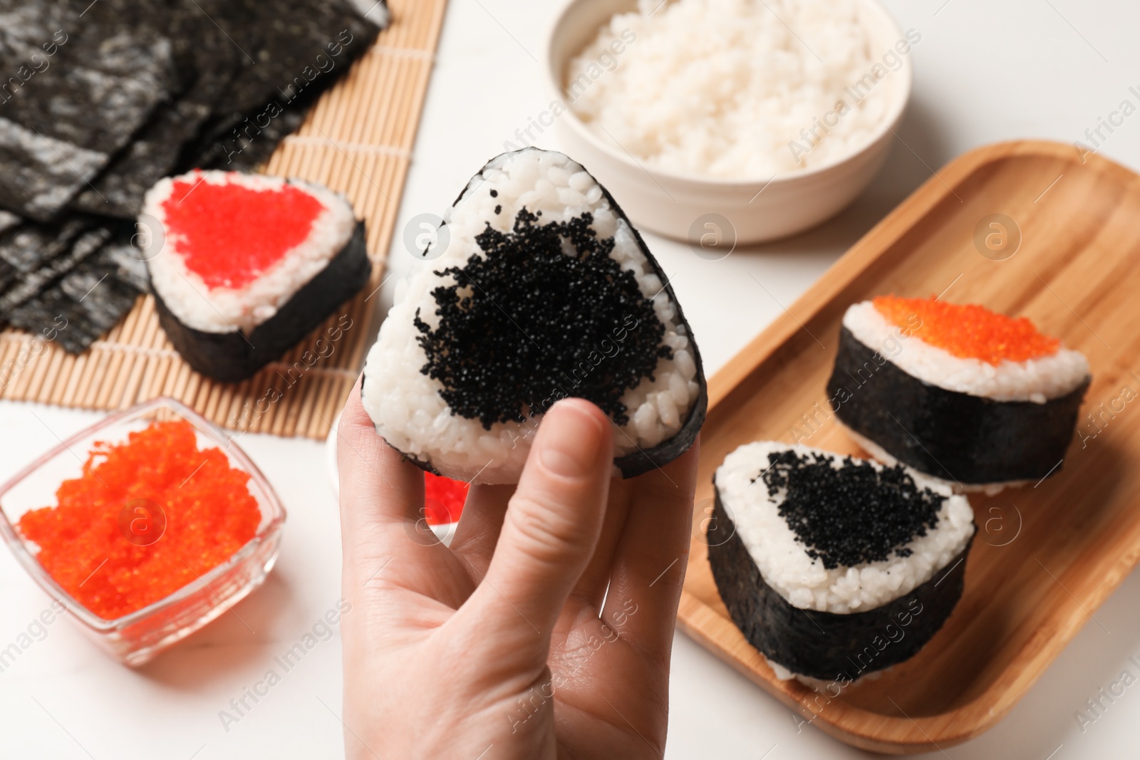 Woman with tasty tobiko onigiri (Japanese rice balls) at white table, closeup Photo of Woman with tasty tobiko onigiri (Japanese rice balls) at white table, closeup