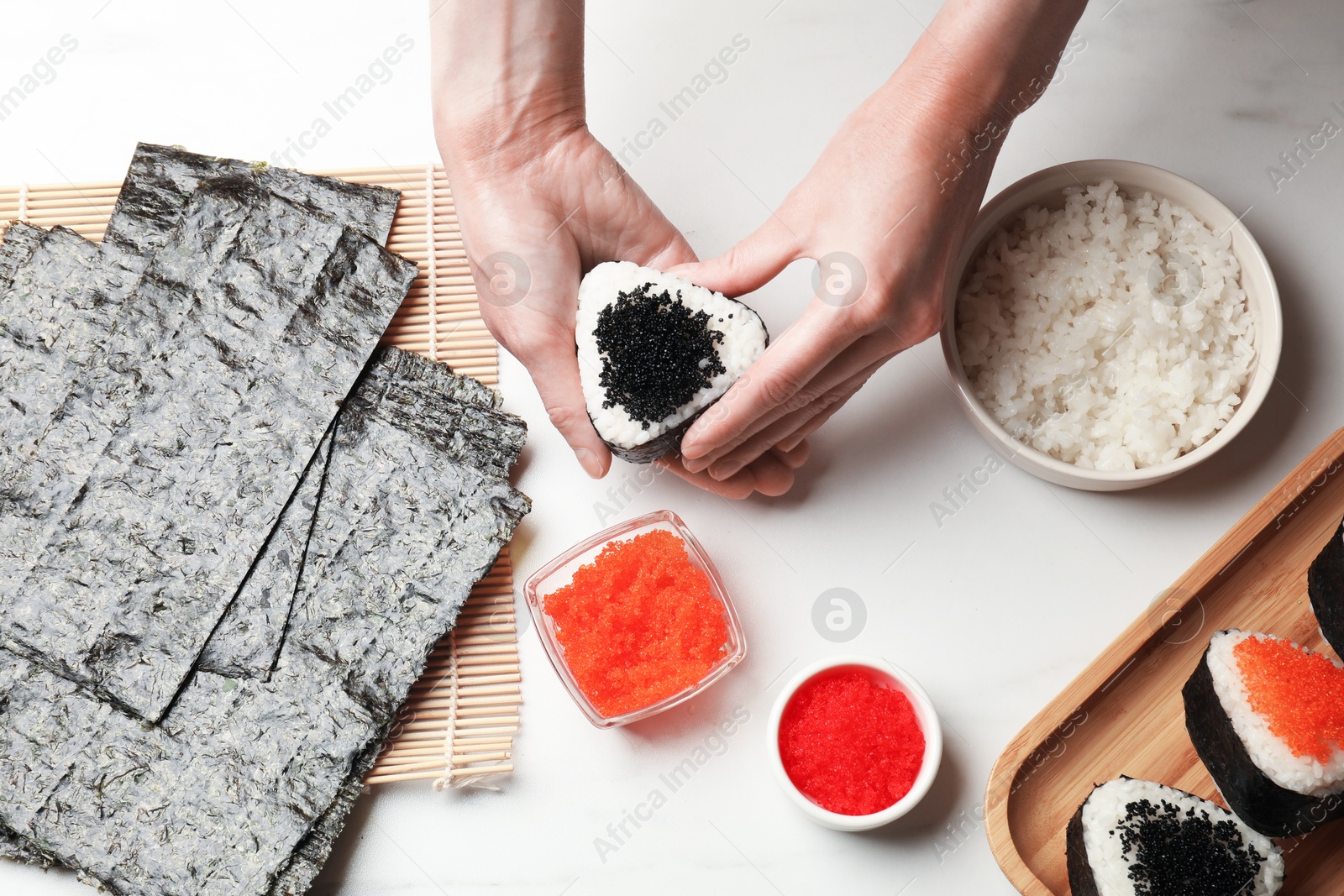 Woman with tasty tobiko onigiri (Japanese rice balls) at white marble table, top view Photo of Woman with tasty tobiko onigiri (Japanese rice balls) at white marble table, top view