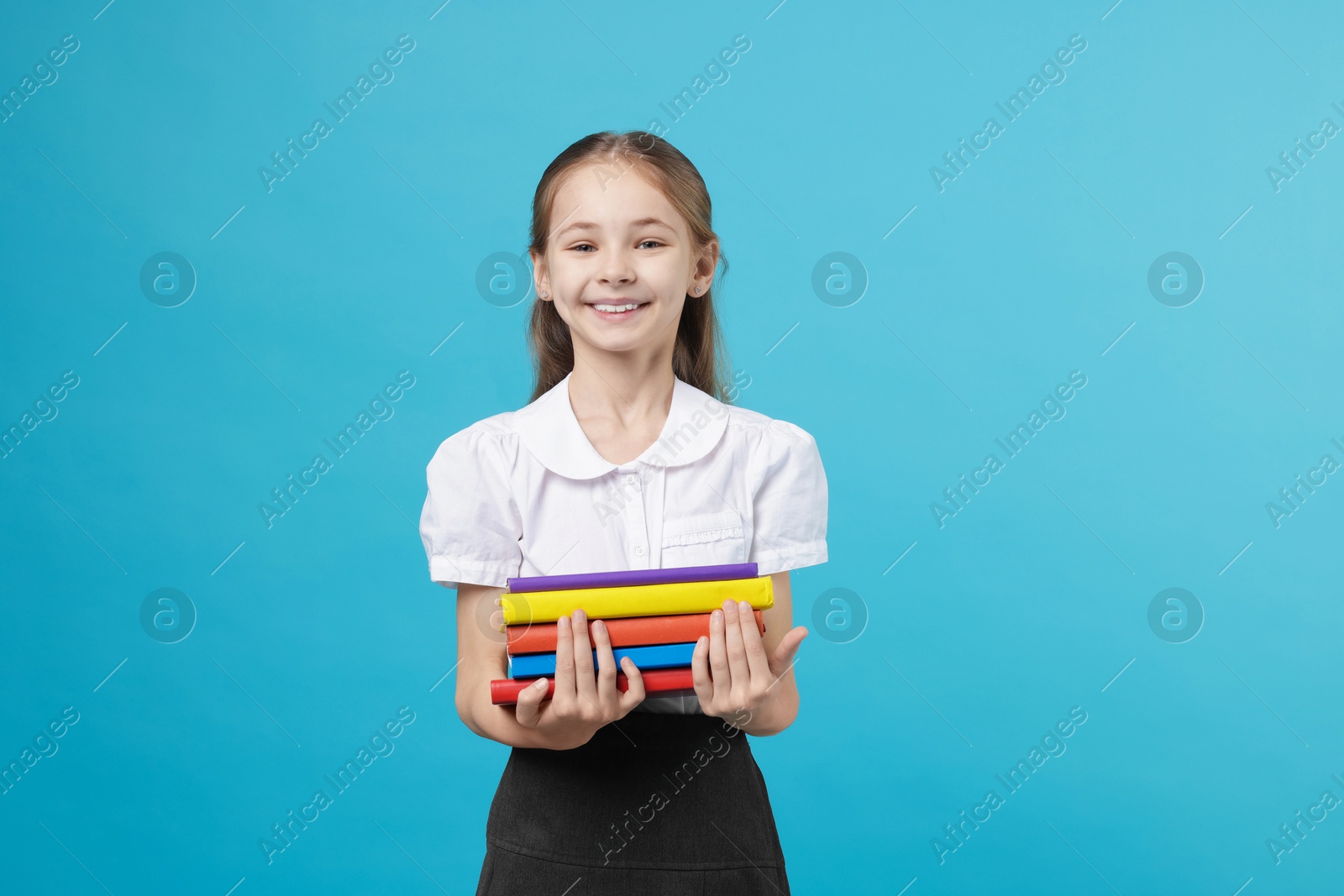 Schoolgirl with books on light blue background Photo of Schoolgirl with books on light blue background
