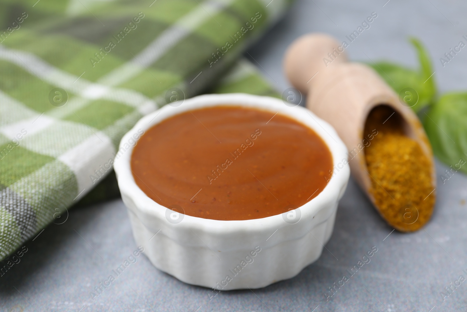 Tasty curry sauce, powder and basil leaves on grey table, closeup Photo of Tasty curry sauce, powder and basil leaves on grey table, closeup