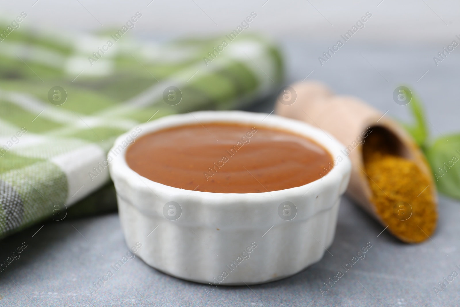 Tasty curry sauce, powder and basil leaves on grey table, closeup Photo of Tasty curry sauce, powder and basil leaves on grey table, closeup