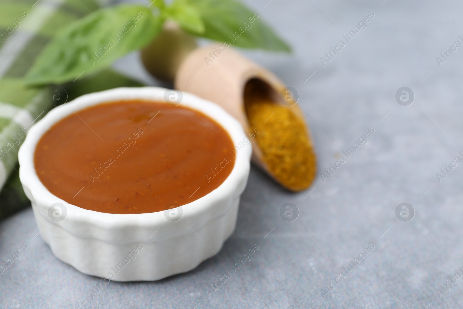 Tasty curry sauce, powder and basil leaves on grey table, closeup. Space for text Photo of Tasty curry sauce, powder and basil leaves on grey table, closeup. Space for text