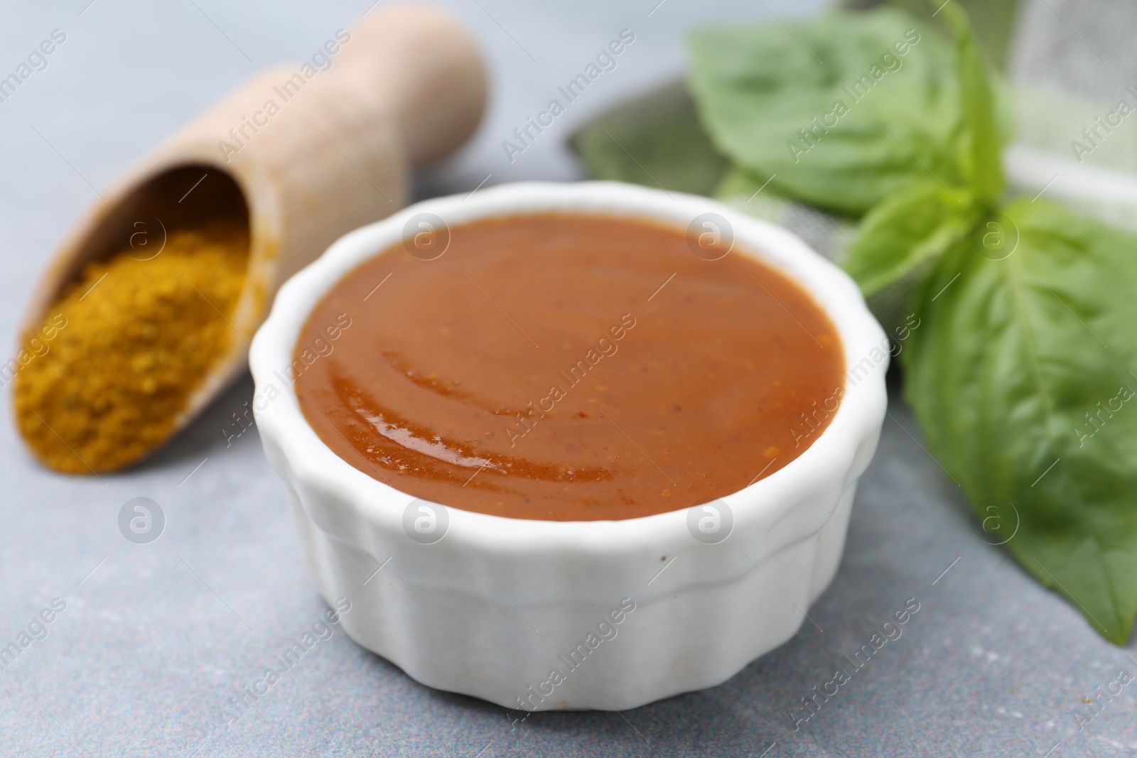Tasty curry sauce, powder and basil leaves on grey table, closeup Photo of Tasty curry sauce, powder and basil leaves on grey table, closeup
