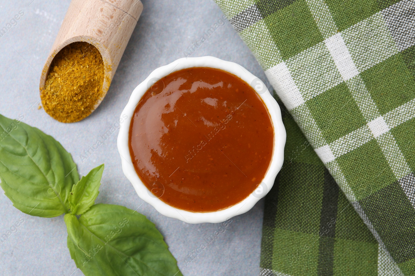 Tasty curry sauce, powder and basil leaves on grey table, flat lay Photo of Tasty curry sauce, powder and basil leaves on grey table, flat lay