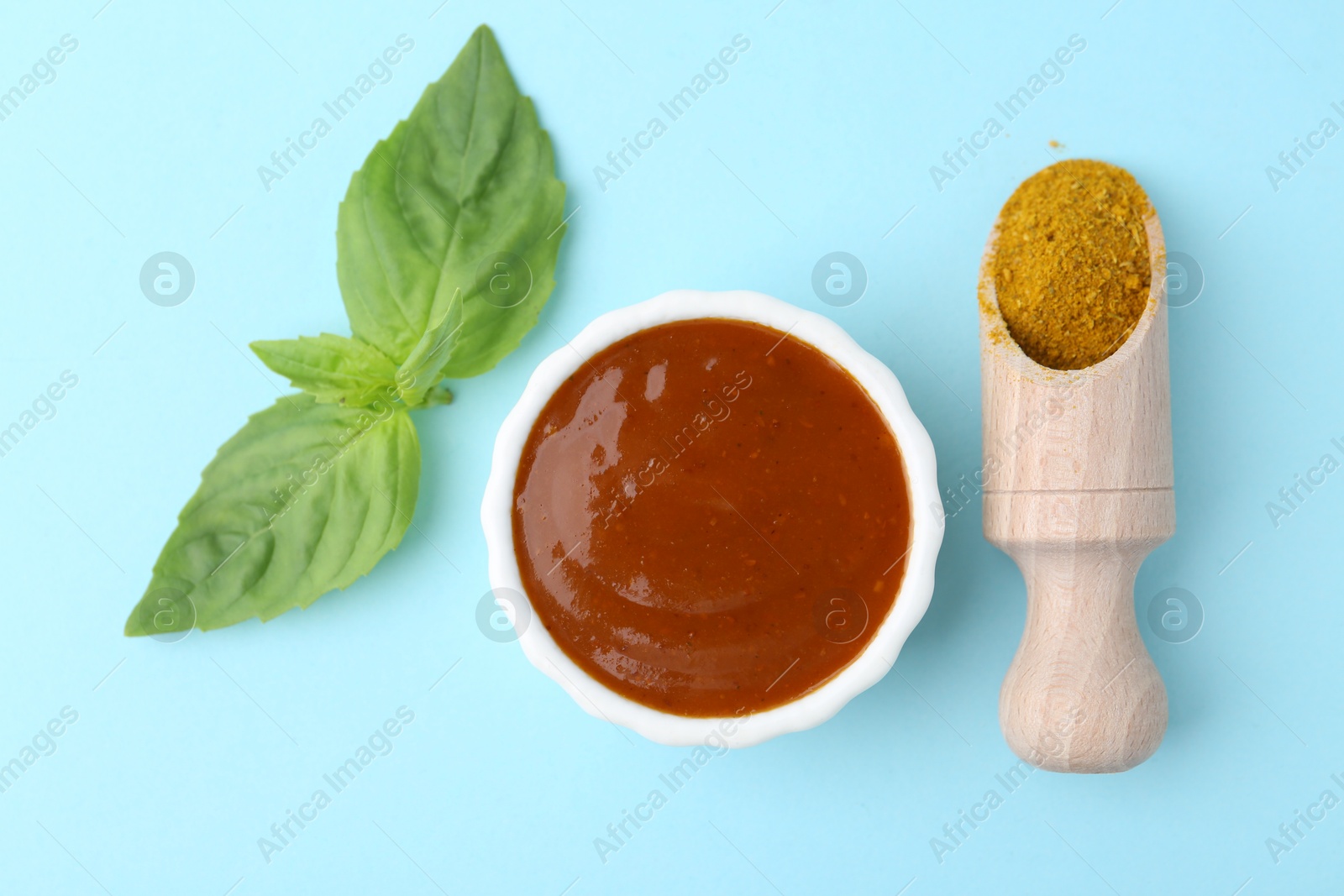 Tasty curry sauce, powder and basil leaves on light blue background, flat lay Photo of Tasty curry sauce, powder and basil leaves on light blue background, flat lay