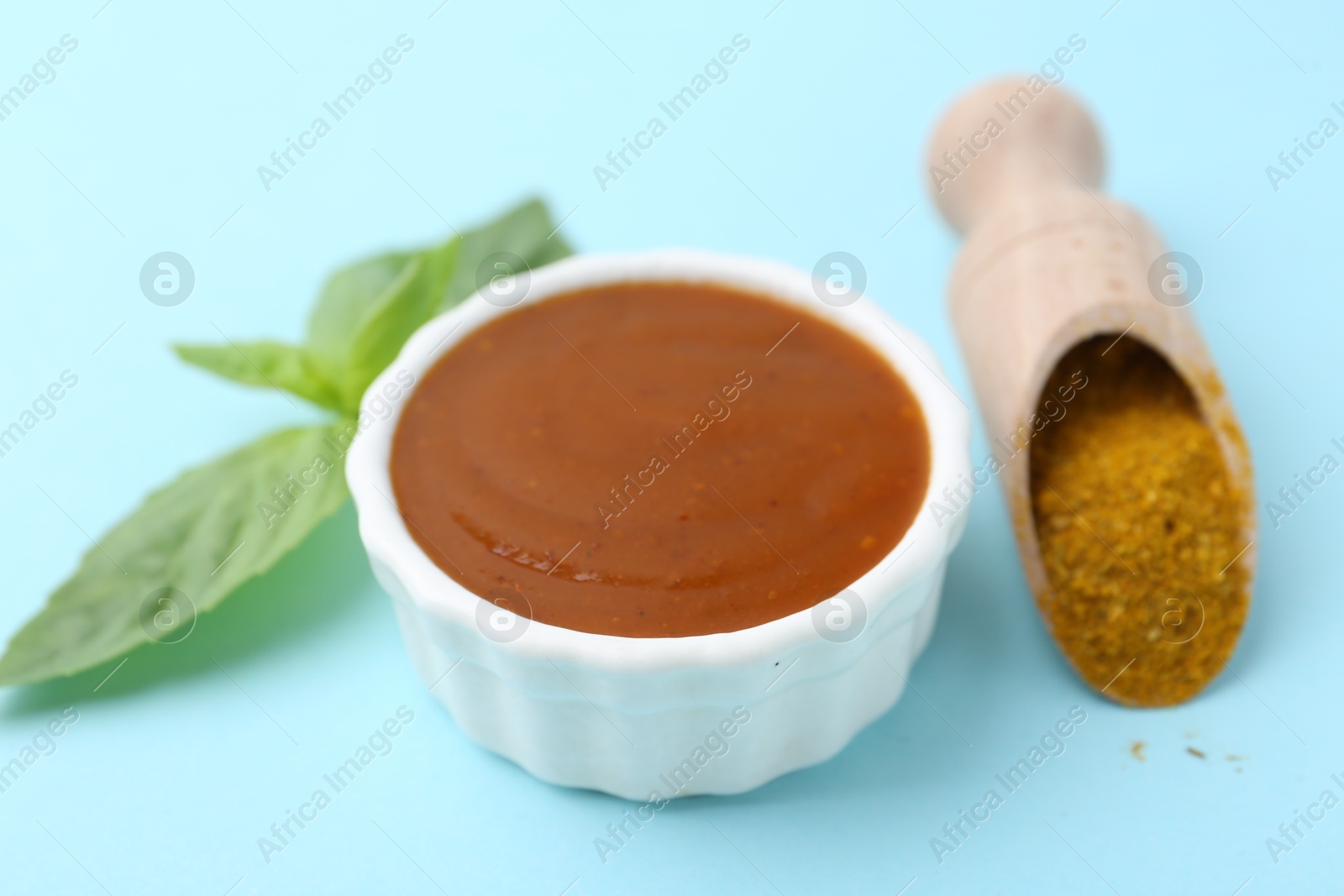 Tasty curry sauce, powder and basil leaves on light blue background, closeup Photo of Tasty curry sauce, powder and basil leaves on light blue background, closeup