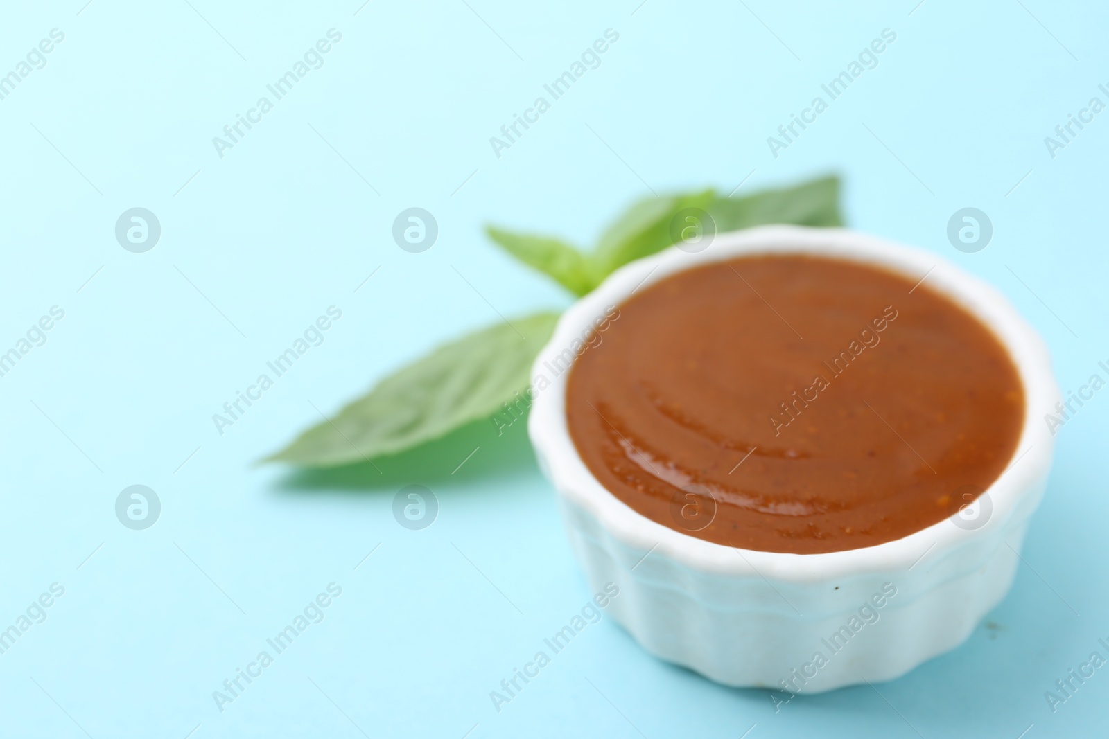 Tasty curry sauce and basil leaves on light blue background, closeup. Space for text Photo of Tasty curry sauce and basil leaves on light blue background, closeup. Space for text
