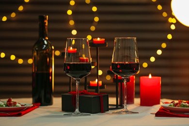 Photo of Red wine, burning candles and gift box on table. Romantic dinner