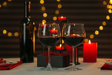 Photo of Red wine, burning candles and gift box on table. Romantic dinner