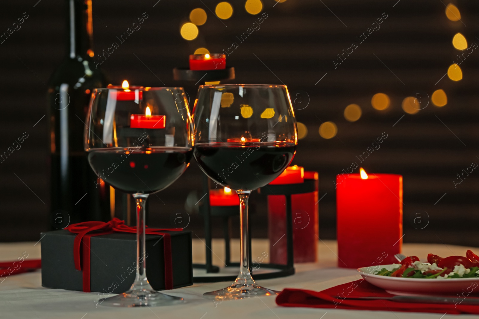 Photo of Red wine, burning candles and gift box on table. Romantic dinner