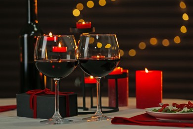 Photo of Red wine, burning candles and gift box on table. Romantic dinner