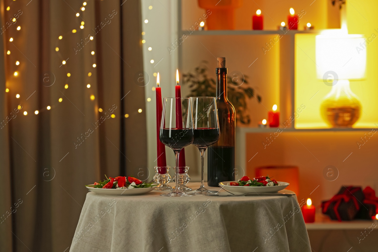 Romantic place setting with red wine and burning candles on table in restaurant Photo of Romantic place setting with red wine and burning candles on table in restaurant