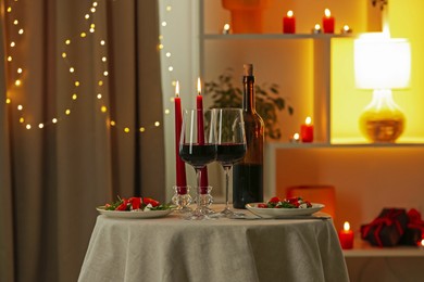 Photo of Romantic place setting with red wine and burning candles on table in restaurant