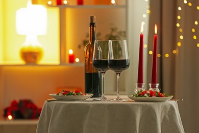 Photo of Romantic place setting with red wine and burning candles on table in restaurant