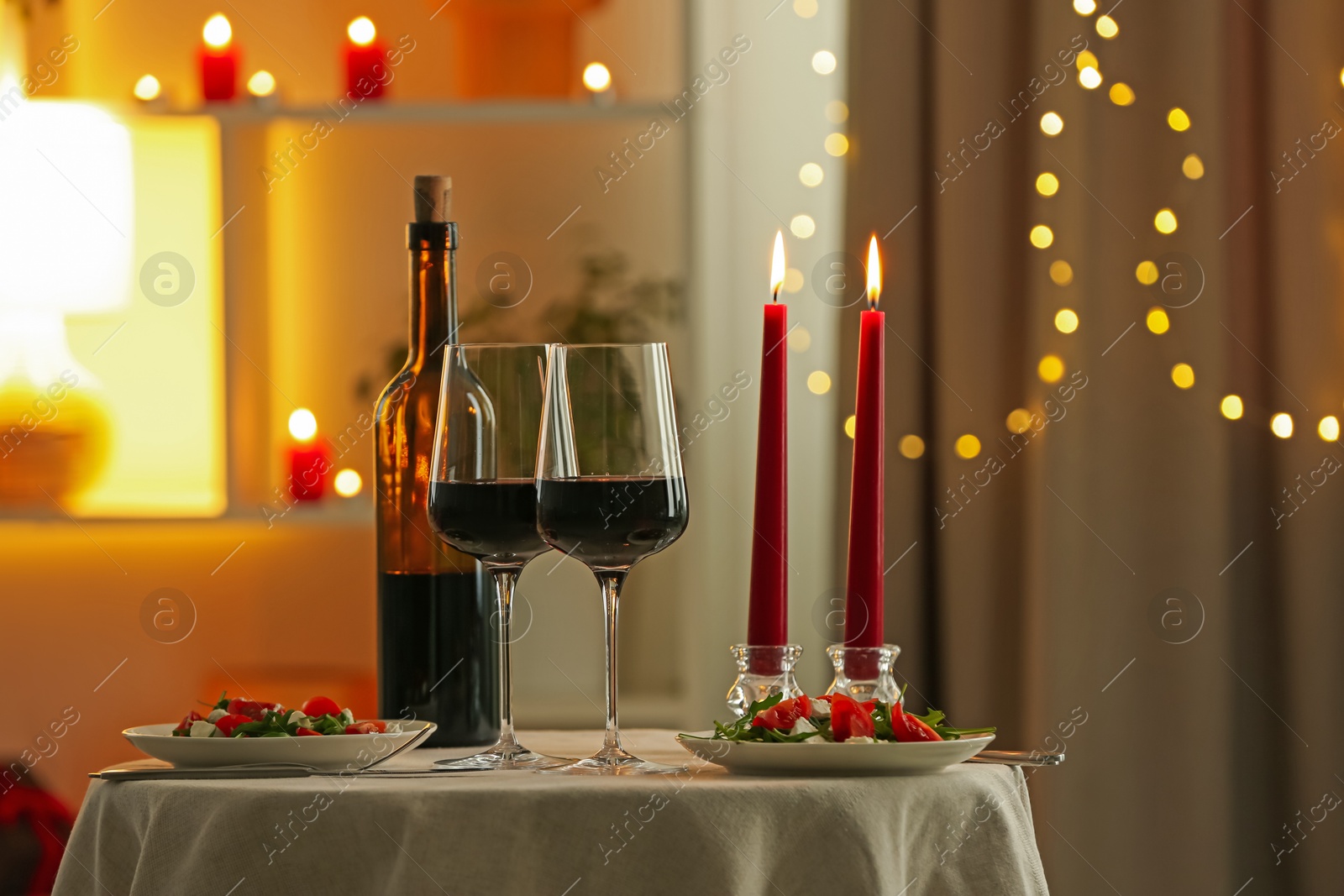 Photo of Romantic place setting with red wine and burning candles on table in restaurant