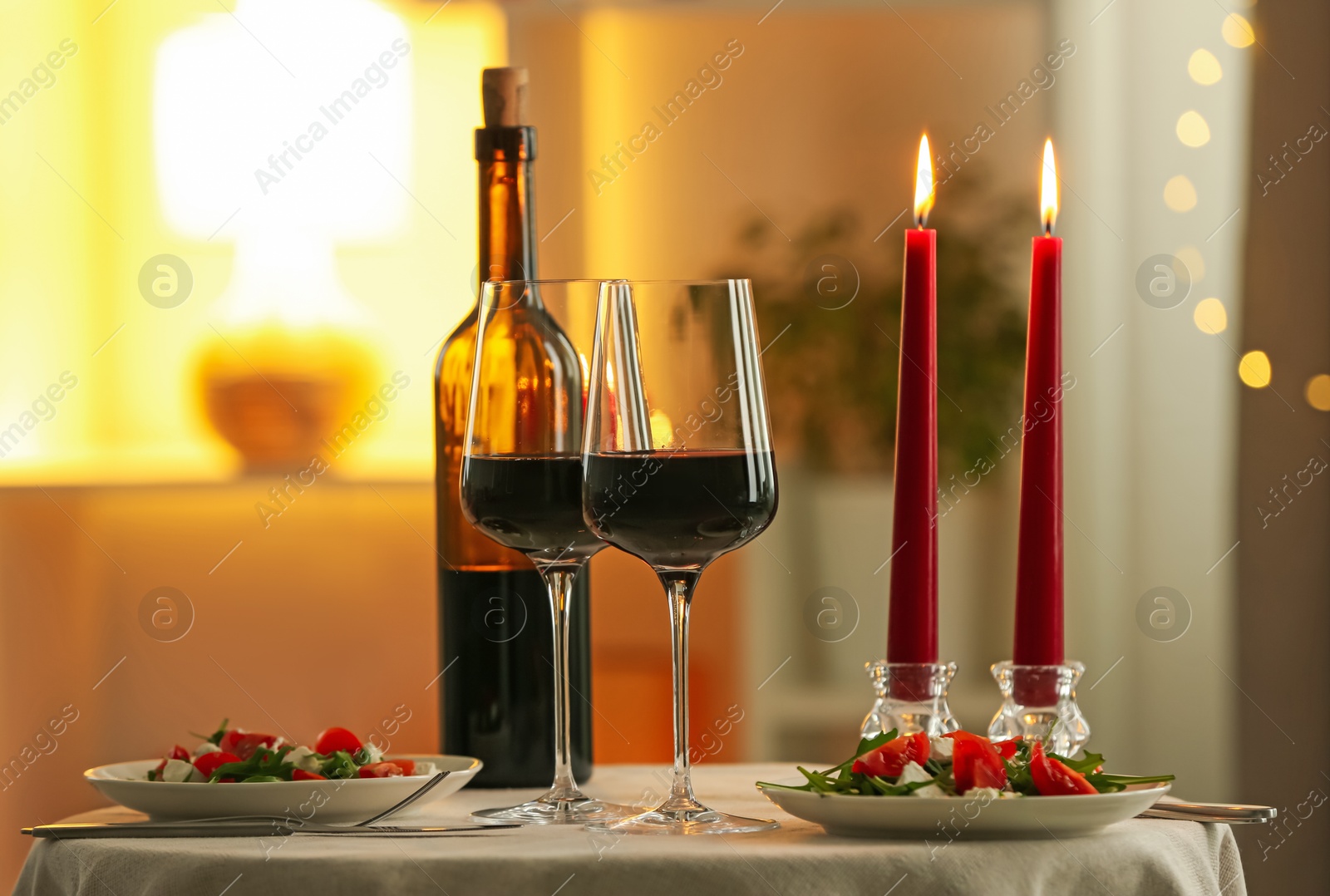 Photo of Romantic place setting with red wine and burning candles on table in restaurant