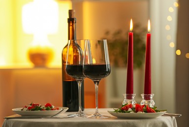 Photo of Romantic place setting with red wine and burning candles on table in restaurant
