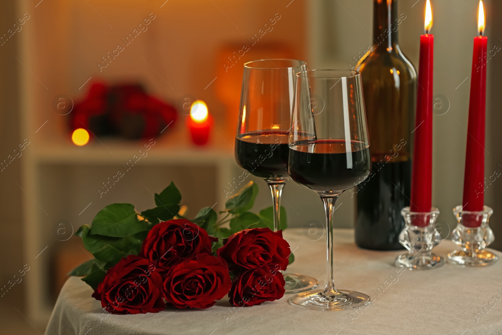 Photo of Glasses of red wine, burning candles and roses on table in restaurant. Romantic dinner