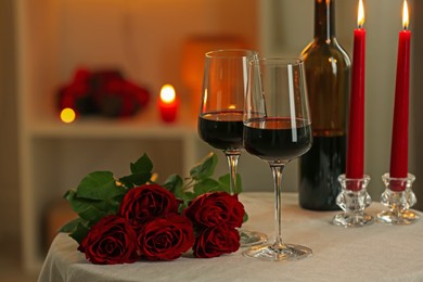 Photo of Glasses of red wine, burning candles and roses on table in restaurant. Romantic dinner