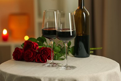 Photo of Glasses of red wine and roses on table in restaurant. Romantic dinner