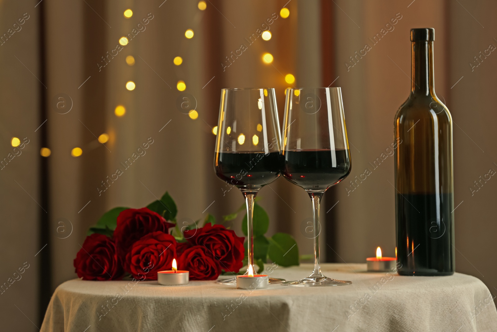 Photo of Glasses of red wine, burning candles and roses on table in restaurant. Romantic dinner