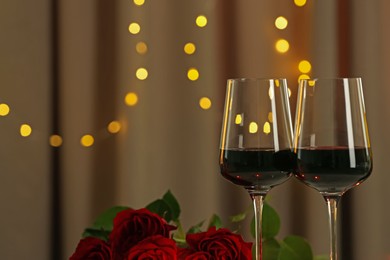 Photo of Romantic dinner. Glasses of red wine against blurred lights, closeup. Space for text