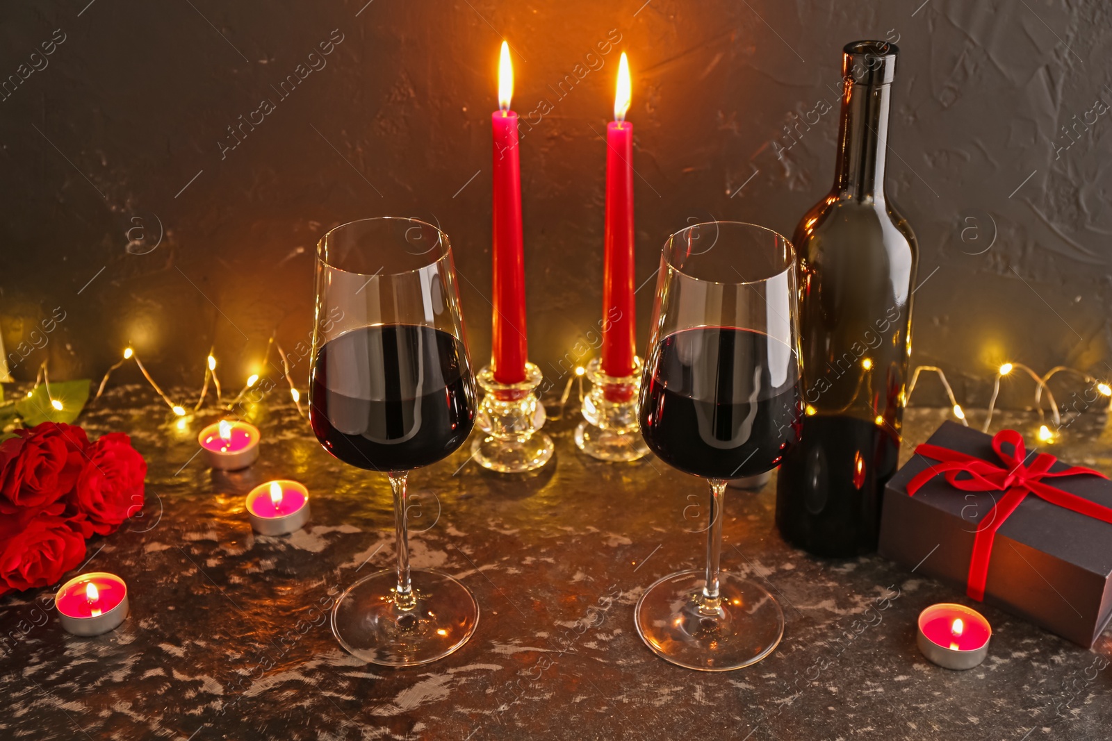Photo of Glasses of wine, burning candles, gift box and roses on black textured table. Romantic dinner
