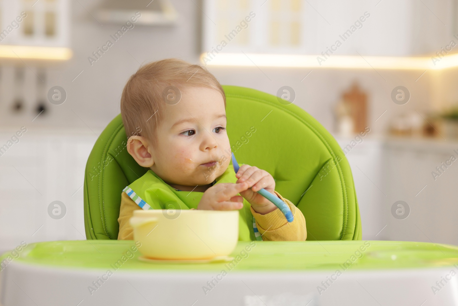 Cute little baby eating healthy food in high chair indoors Photo of Cute little baby eating healthy food in high chair indoors