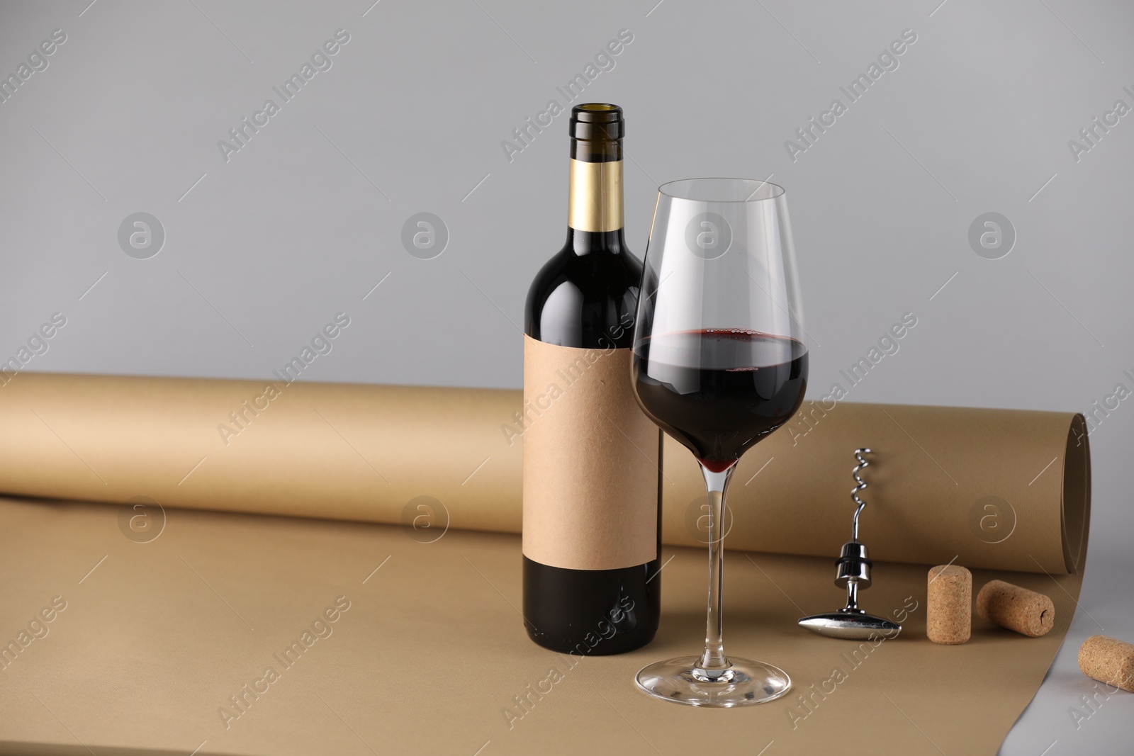 Photo of Bottle and glass of wine with corkscrew, corks and paper on grey background. Space for text