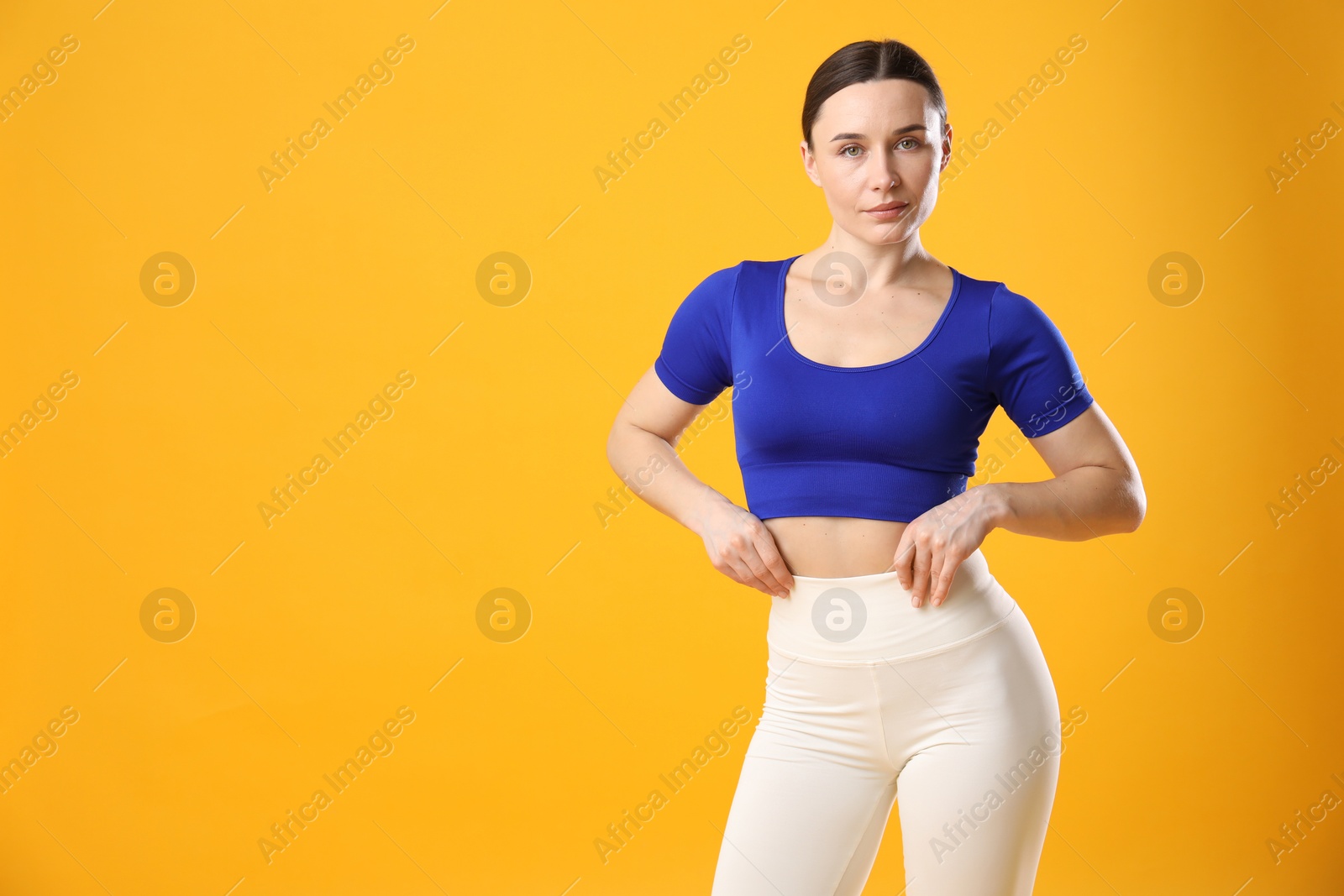 Woman in sportswear posing on orange background, space for text Photo of Woman in sportswear posing on orange background, space for text