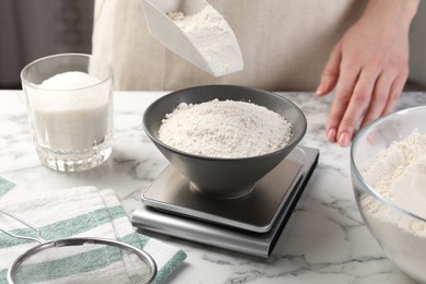 Photo of Woman putting sugar into bowl on digital kitchen scale at white marble table, closeup