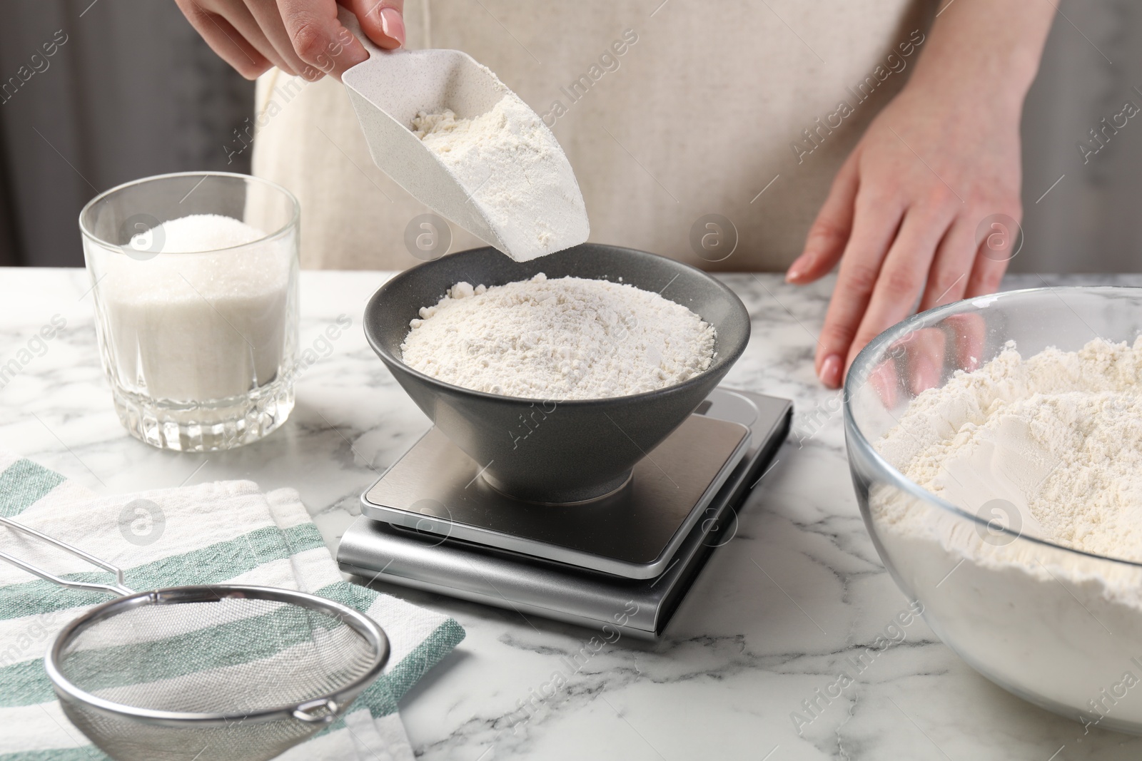 Woman putting sugar into bowl on digital kitchen scale at white marble table, closeup Photo of Woman putting sugar into bowl on digital kitchen scale at white marble table, closeup
