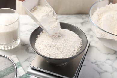 Photo of Woman putting sugar into bowl on digital kitchen scale at white marble table, closeup