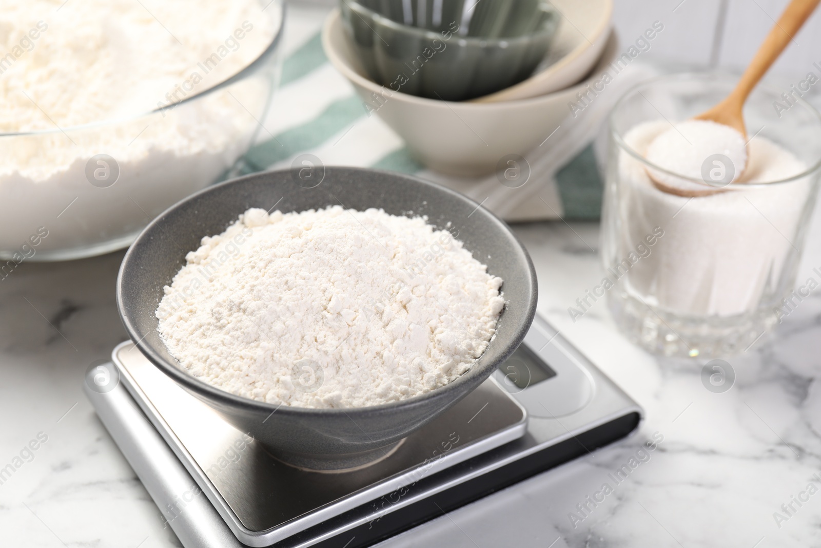 Digital kitchen scale with bowl of flour and other products on white marble table, closeup Photo of Digital kitchen scale with bowl of flour and other products on white marble table, closeup