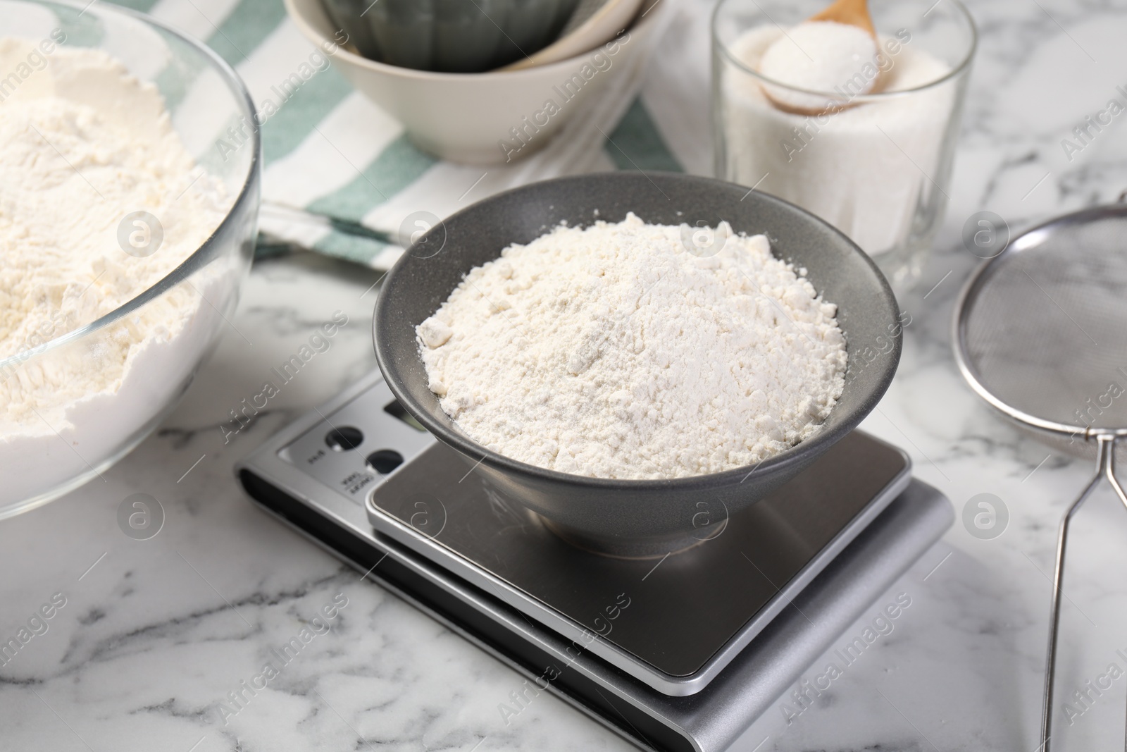Digital kitchen scale with bowl of flour and other products on white marble table, closeup Photo of Digital kitchen scale with bowl of flour and other products on white marble table, closeup