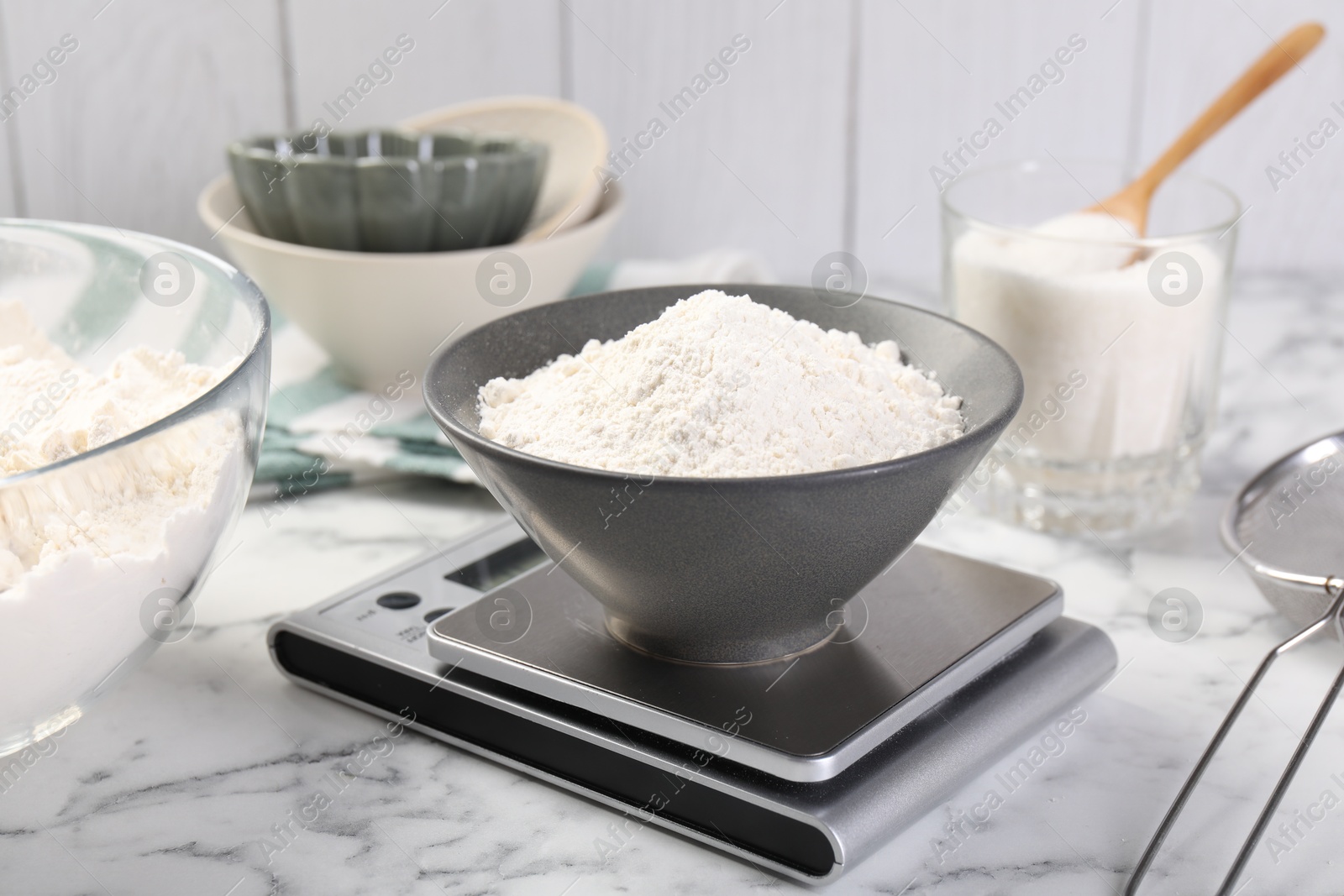 Digital kitchen scale with bowl of flour and other products on white marble table, closeup Photo of Digital kitchen scale with bowl of flour and other products on white marble table, closeup