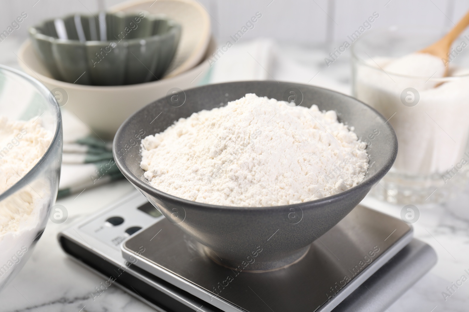 Digital kitchen scale with bowl of flour and other products on white marble table, closeup Photo of Digital kitchen scale with bowl of flour and other products on white marble table, closeup