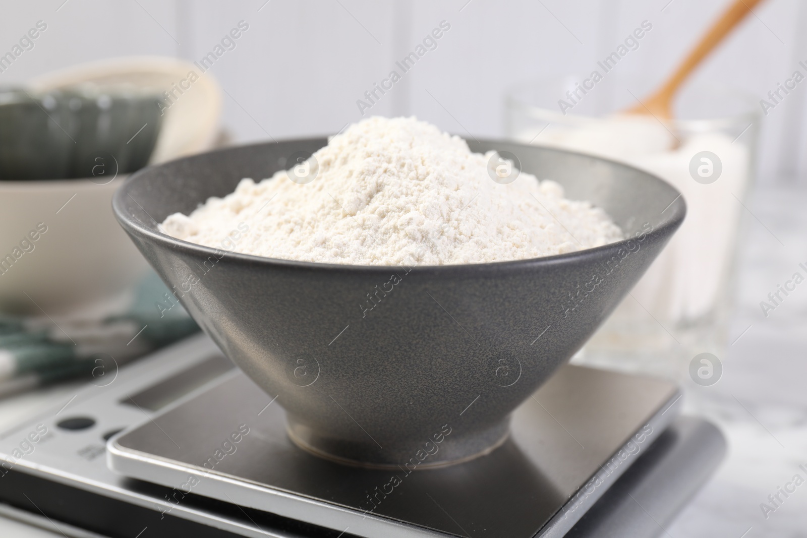Digital kitchen scale with bowl of flour and other products on white marble table, closeup Photo of Digital kitchen scale with bowl of flour and other products on white marble table, closeup
