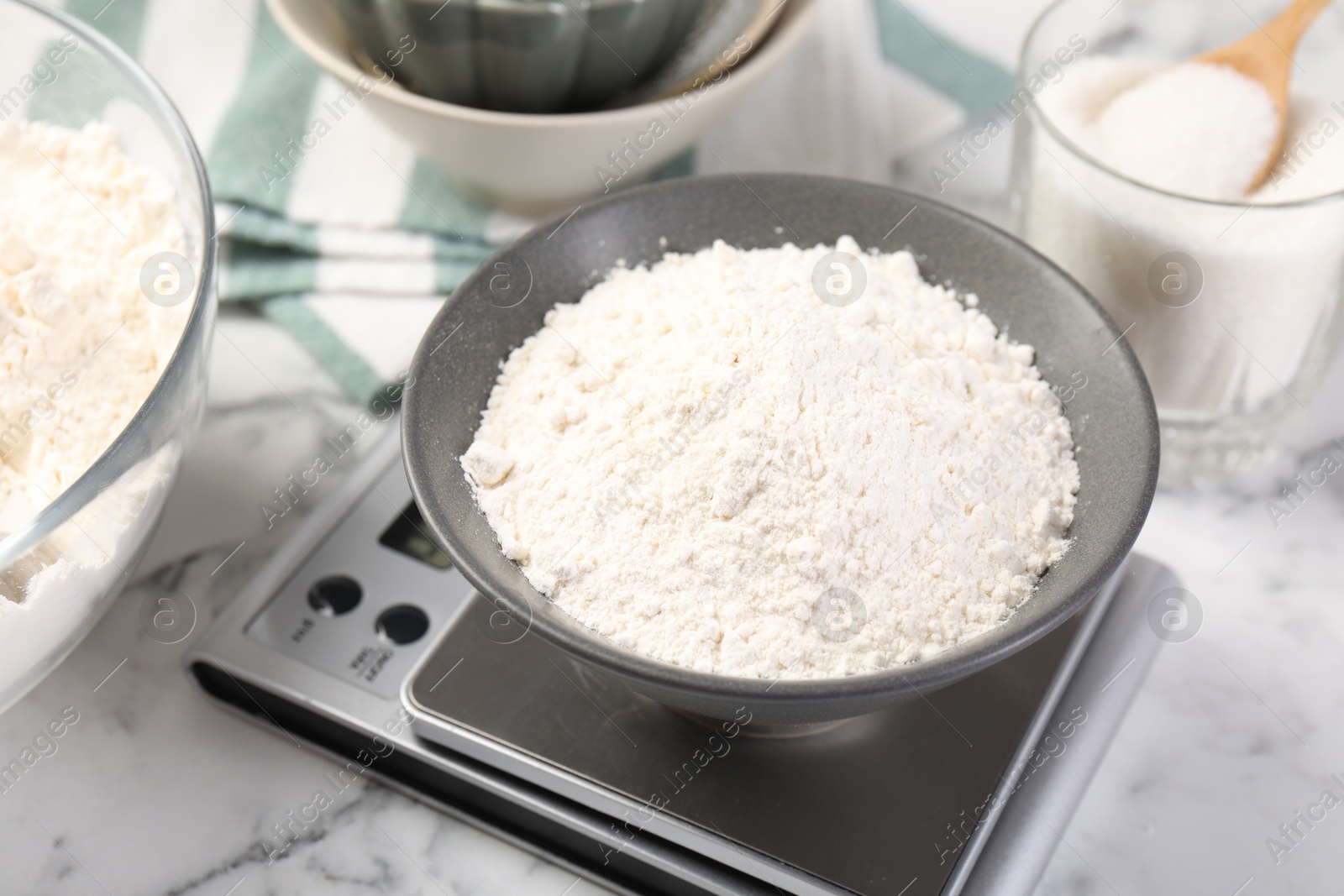 Digital kitchen scale with bowl of flour and other products on white marble table, closeup Photo of Digital kitchen scale with bowl of flour and other products on white marble table, closeup
