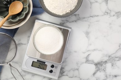 Photo of Digital kitchen scale with glass of sugar and other products on white marble table, flat lay. Space for text