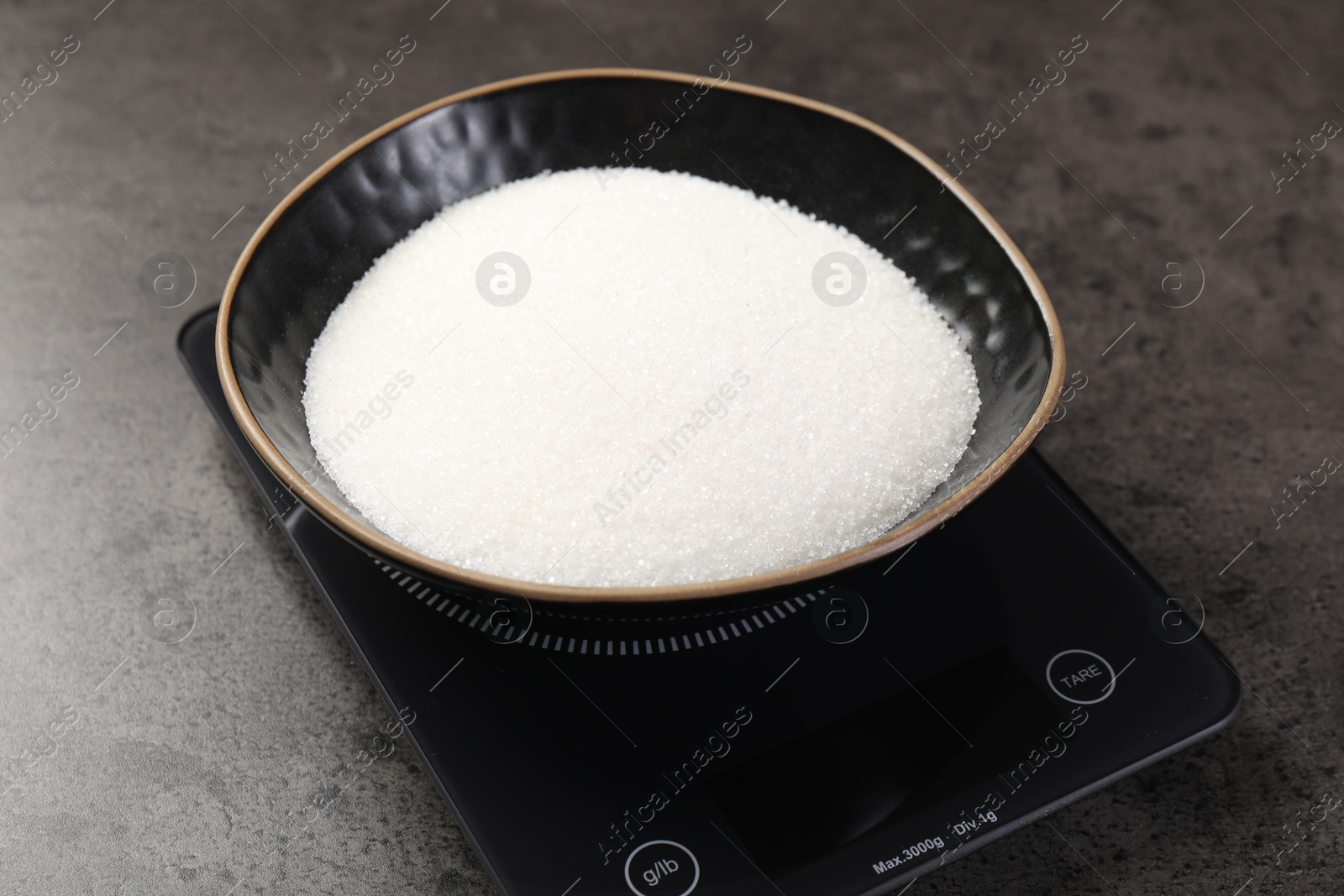 Digital kitchen scale with bowl of sugar on grey table, closeup Photo of Digital kitchen scale with bowl of sugar on grey table, closeup