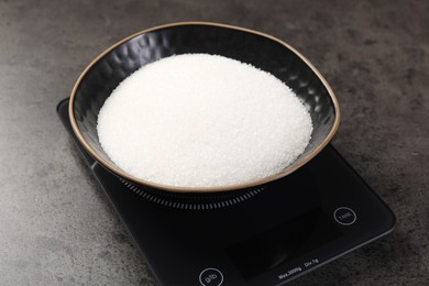 Photo of Digital kitchen scale with bowl of sugar on grey table, closeup