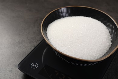 Photo of Digital kitchen scale with bowl of sugar on grey table, closeup