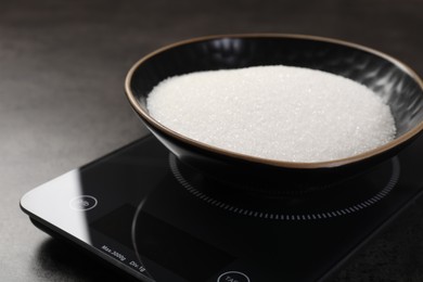 Photo of Digital kitchen scale with bowl of sugar on grey table, closeup