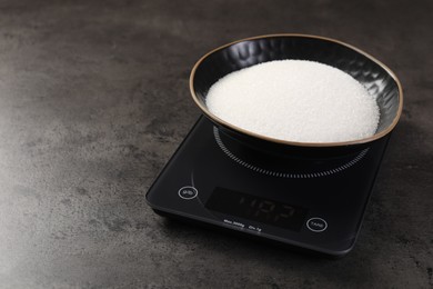 Photo of Digital kitchen scale with bowl of sugar on grey table, closeup. Space for text