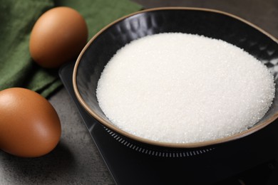 Photo of Digital kitchen scale with bowl of sugar and other products on grey table, closeup