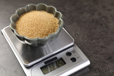 Photo of Digital kitchen scale with bowl of brown sugar on grey table, closeup. Space for text