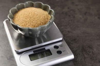 Photo of Digital kitchen scale with bowl of brown sugar on grey table, closeup. Space for text
