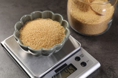 Photo of Digital kitchen scale with bowl of brown sugar on grey table, closeup