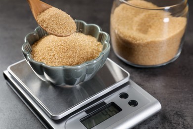Photo of Putting brown sugar into bowl on digital kitchen scale at grey table, closeup